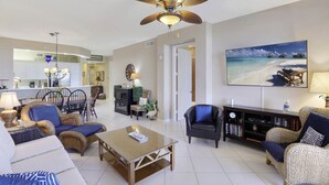 A spacious living room with a ceiling fan, a large flat-screen TV, and a dining area with wicker furniture. - Walk to the Beach (Naples)