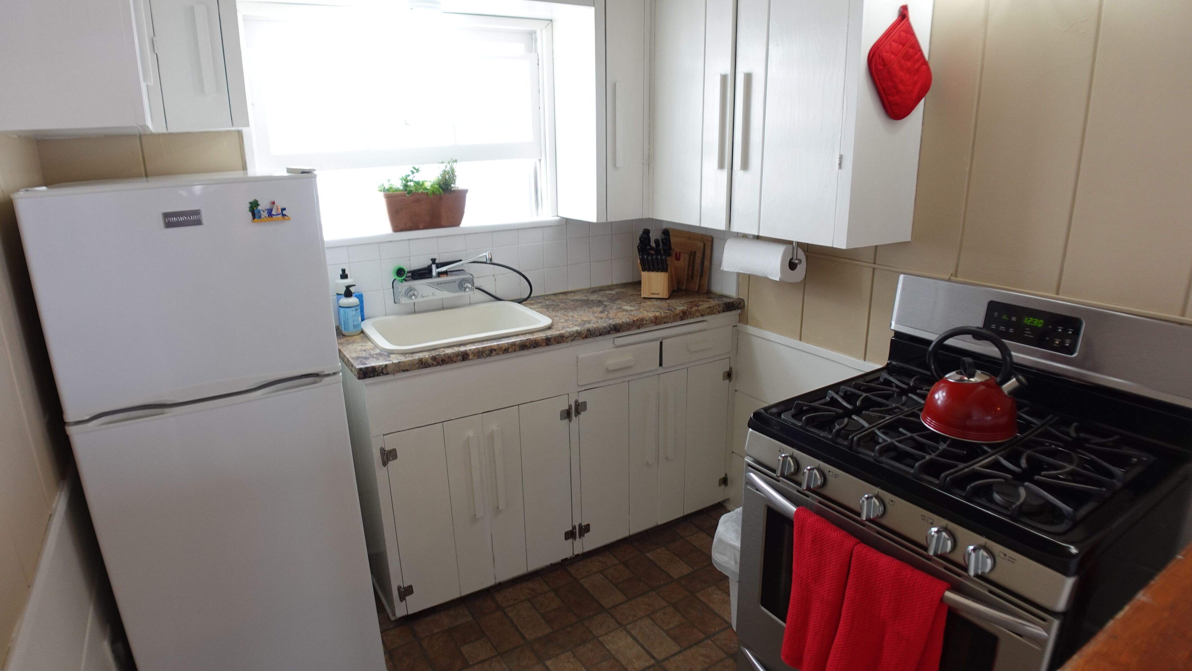 Una cocina con gabinetes blancos, estufa de acero inoxidable, un lavamanos y un refrigerador.