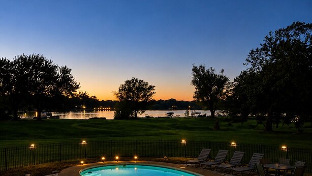 A swimming pool with a curved edge, surrounded by a stone deck and a fence.