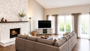 A living room with a fireplace, a sofa, a TV, and a large window with curtains.
