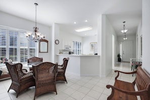 A dining area with wicker chairs, a glass table, and a chandelier.