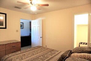 Ein Schlafzimmer mit einem Bett, einem Schminktisch, einem Deckenventilator und einer Tür zu einem anderen Raum.