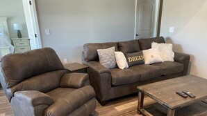 Un sofá de cuero marrón con un sillón a juego y una mesa de centro de madera en una sala de estar con suelo de madera.
