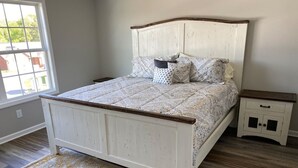 Un dormitorio con cama blanca, ropa de cama estampada, cabecera de madera, mesita de noche y alfombra con diseño.