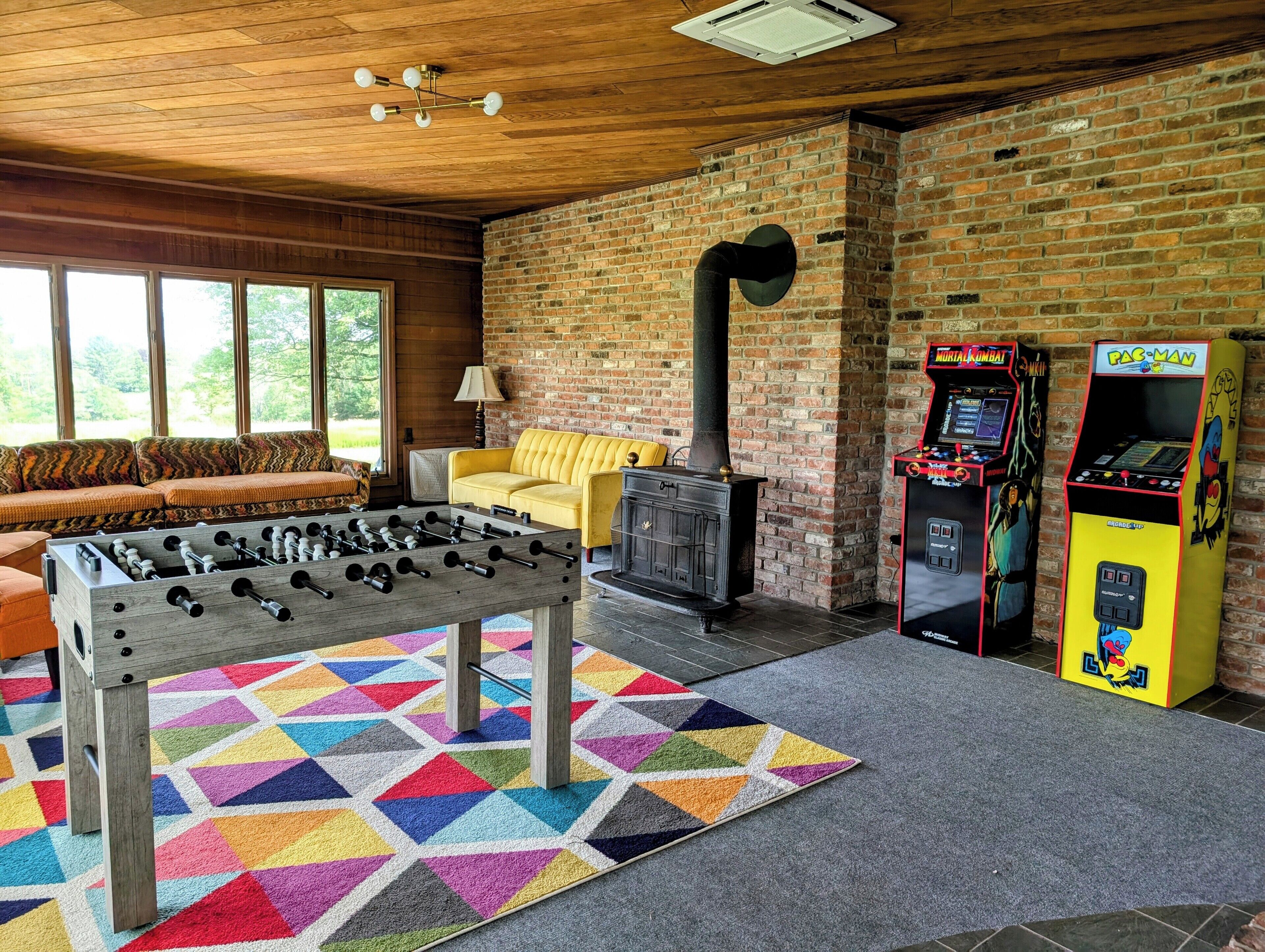 Una habitación acogedora con una mesa de fútbol de mesa, un sofá amarillo y dos máquinas de videojuegos.
