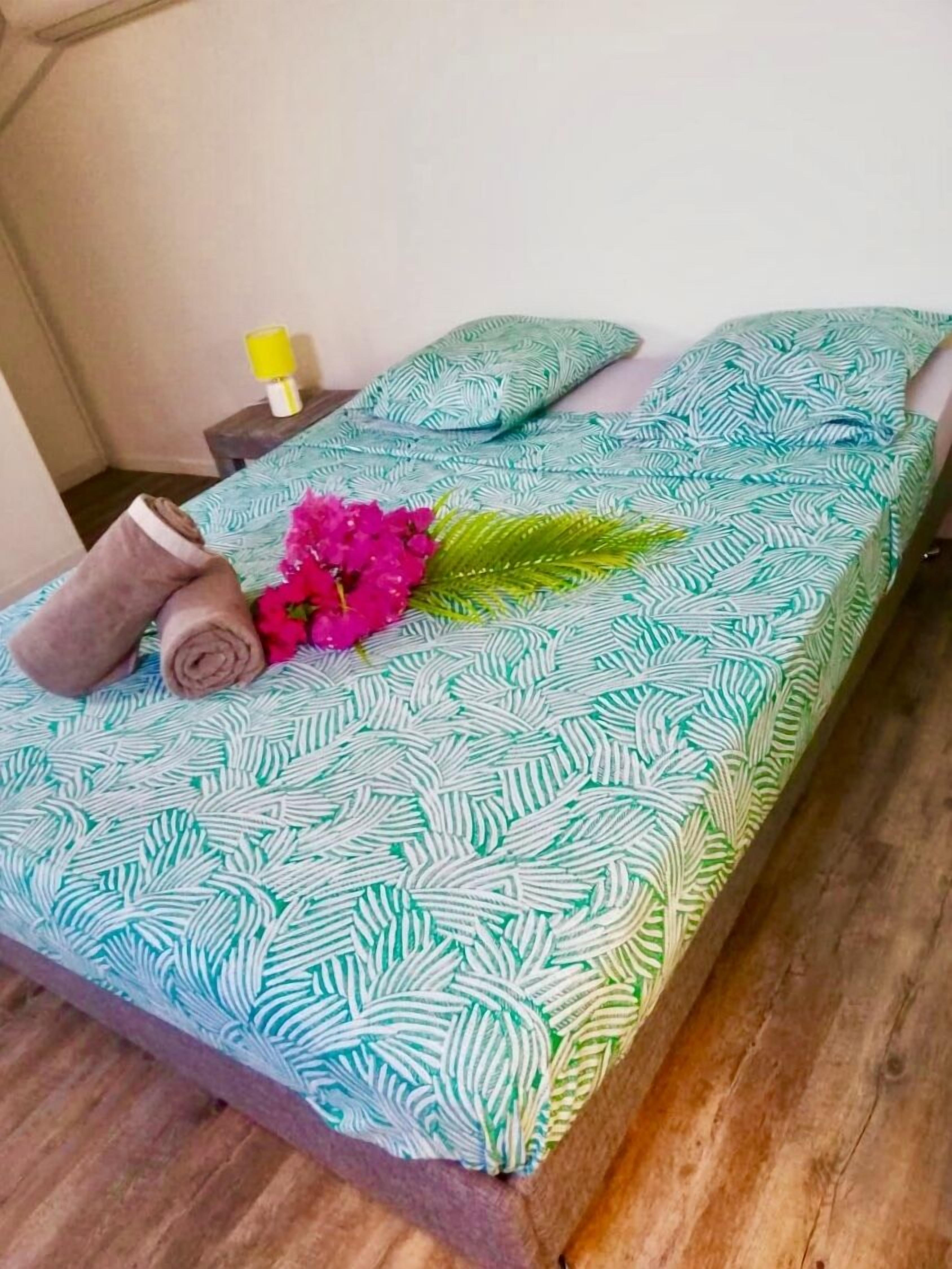 Un llit ben fet amb un estovat estampat, una tovallola arremolinada i un ram de flors.
