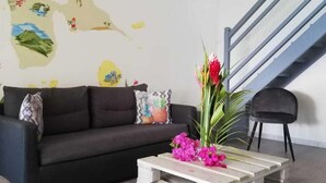 A living room with a dark sofa, a wooden coffee table with flowers, a map on the wall, and a staircase. - LE FLAMBOYANT, triplex sea view, 3 bedrooms, residence with swimming pool (le Gosier)
