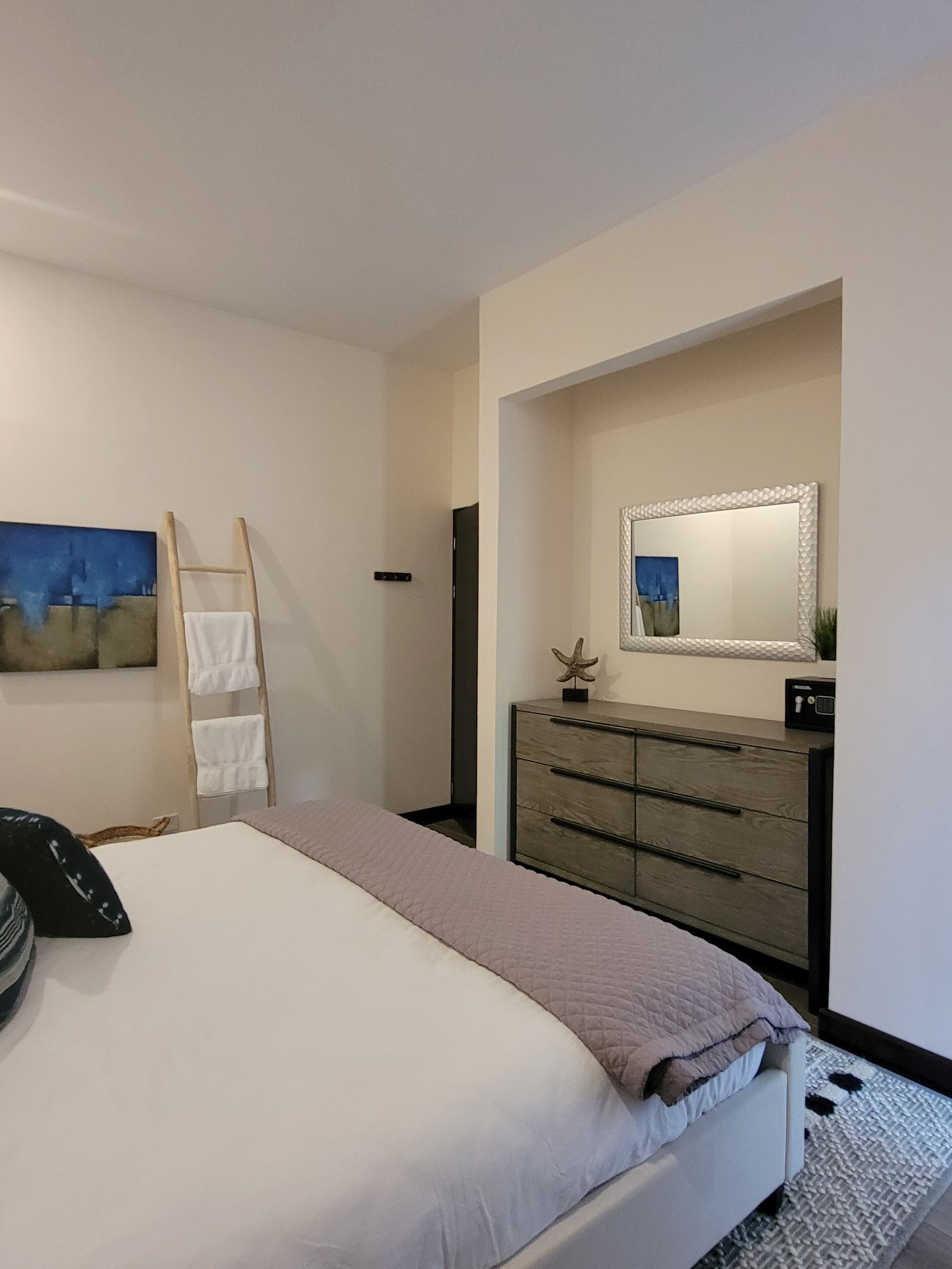 A bedroom with a bed, a dresser, a mirror, and a painting on the wall.