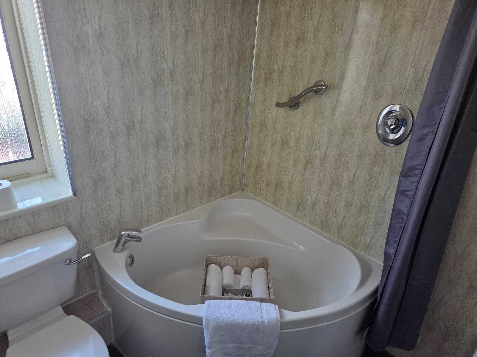 A bathroom with a bathtub, toilet, and a window.