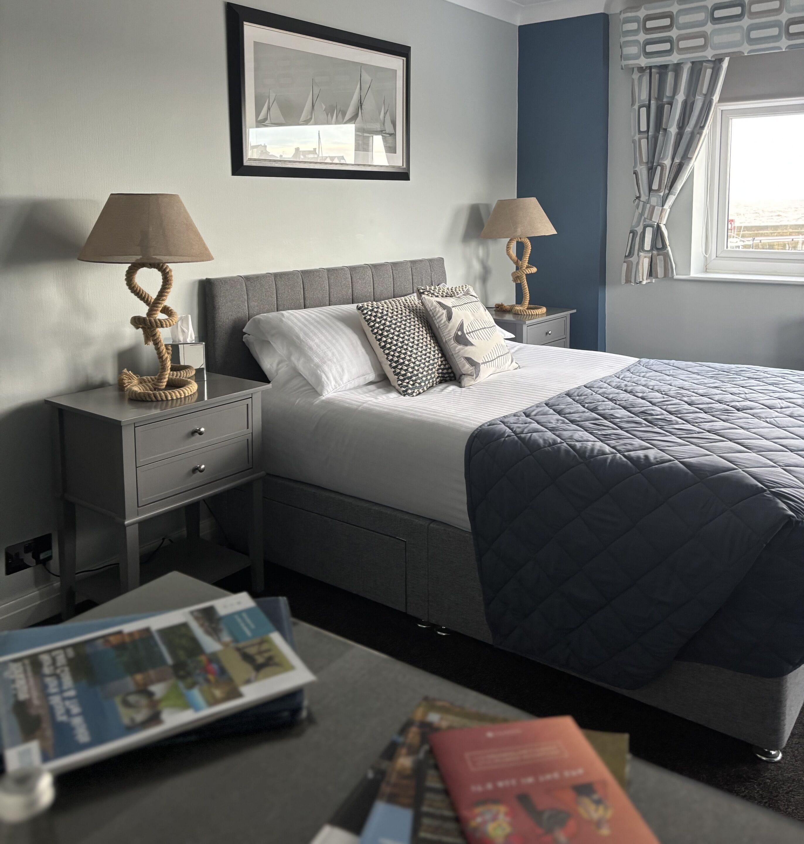 A neatly arranged bedroom with a bed, two bedside tables with lamps, a framed picture on the wall, and a window with curtains.