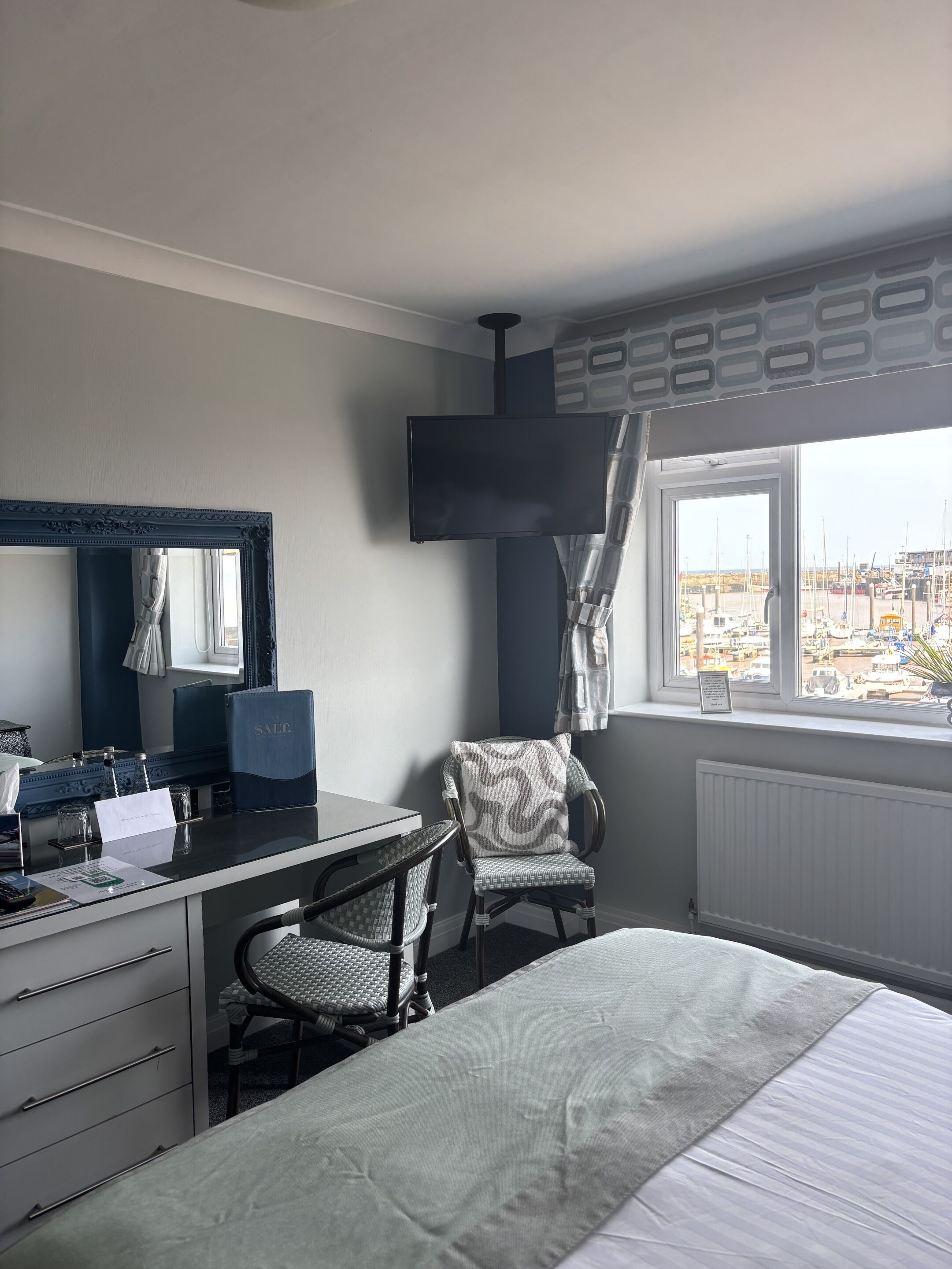A hotel room with a bed, a desk with a computer, a chair, a large mirror, and a window with a view of the city.