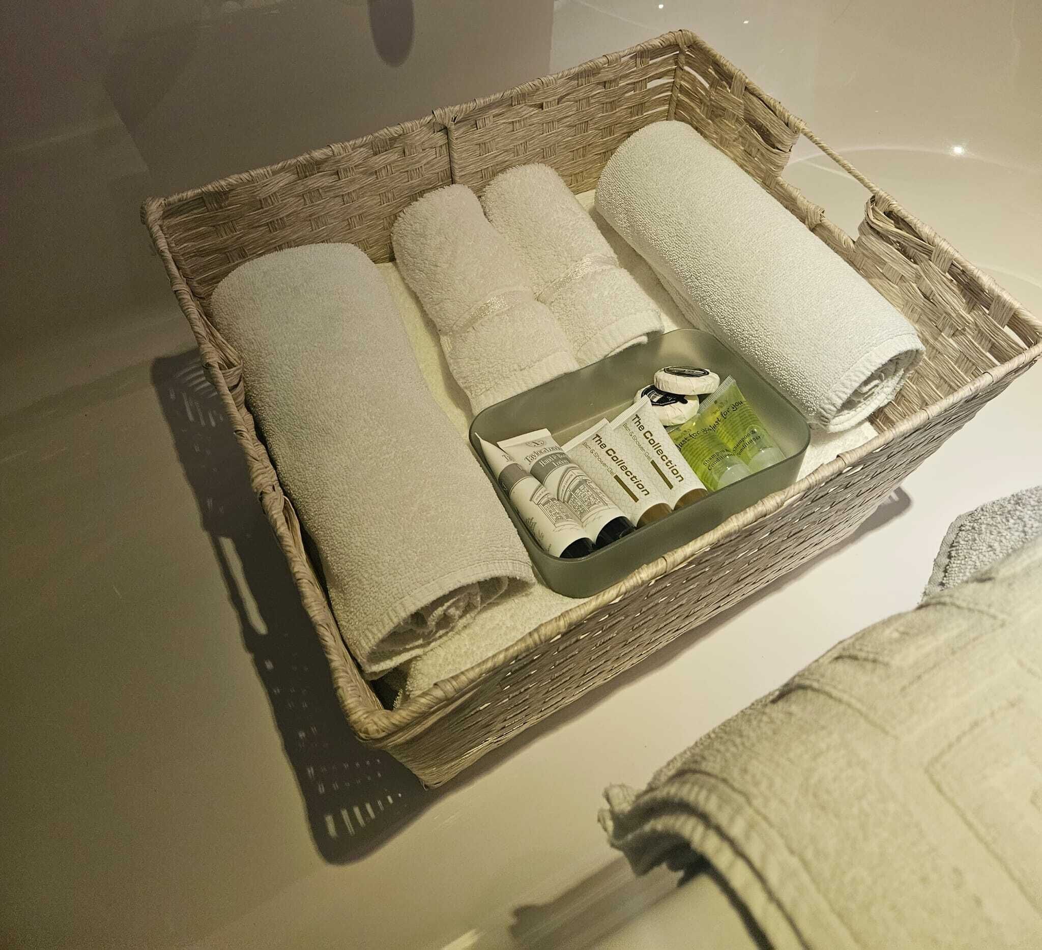 A wicker basket containing rolled towels, a bottle of lotion, and a small booklet.