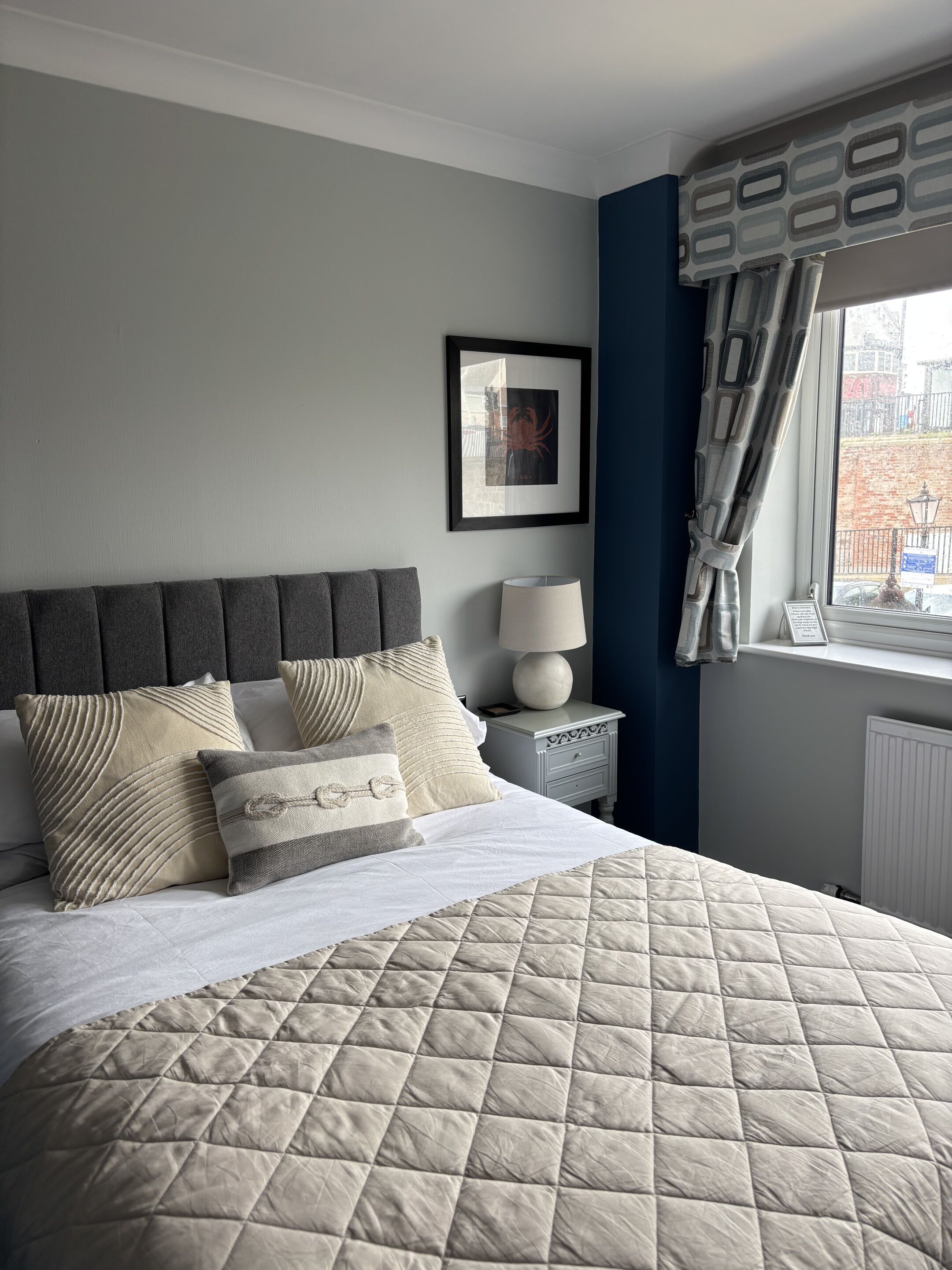Een netjes opgemaakt bed met een gewatteerde spreideken, een bedlampje en een ingelijst foto op de muur.