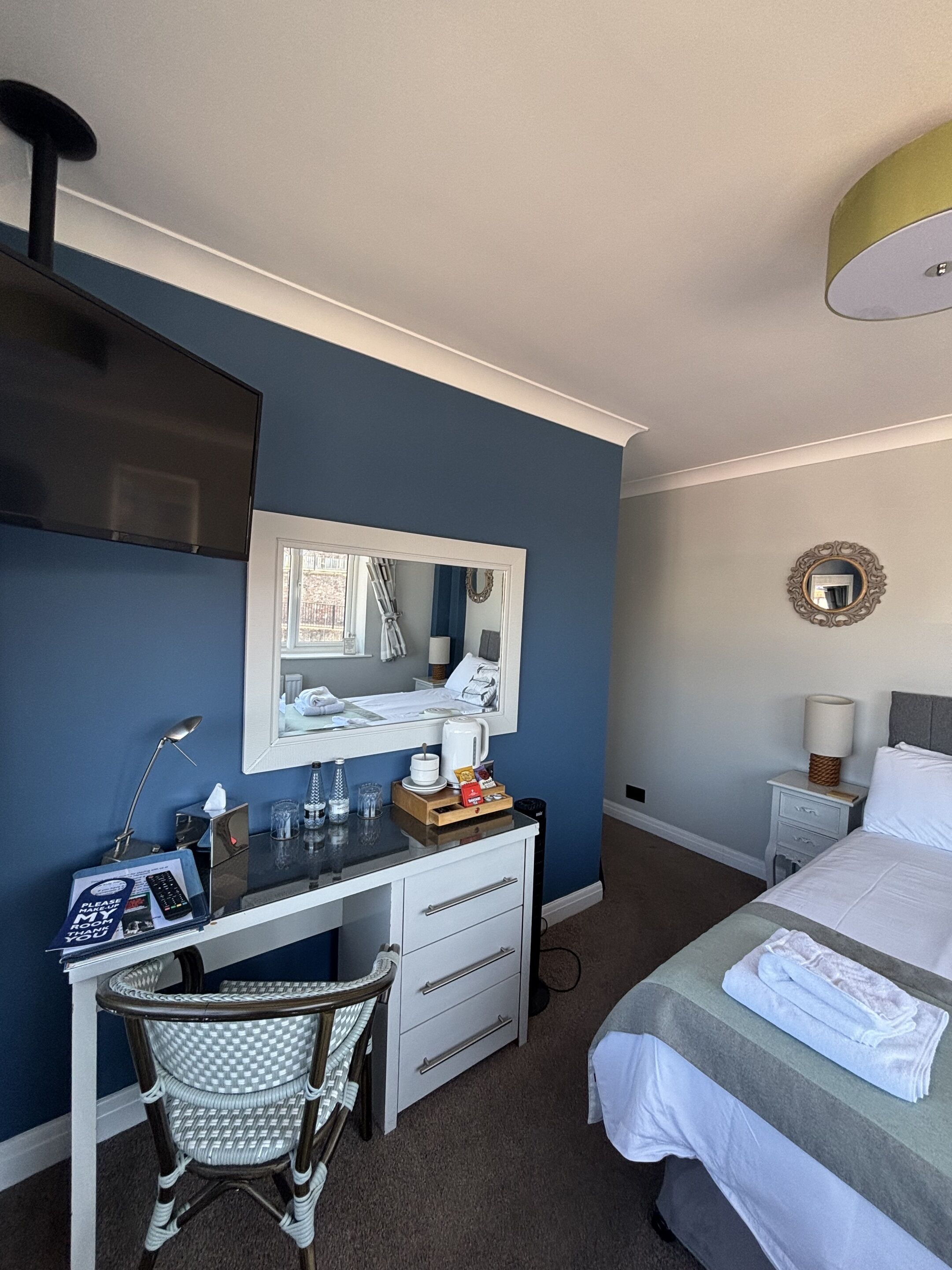 A hotel room with a desk, chair, bed, and a large mirror.