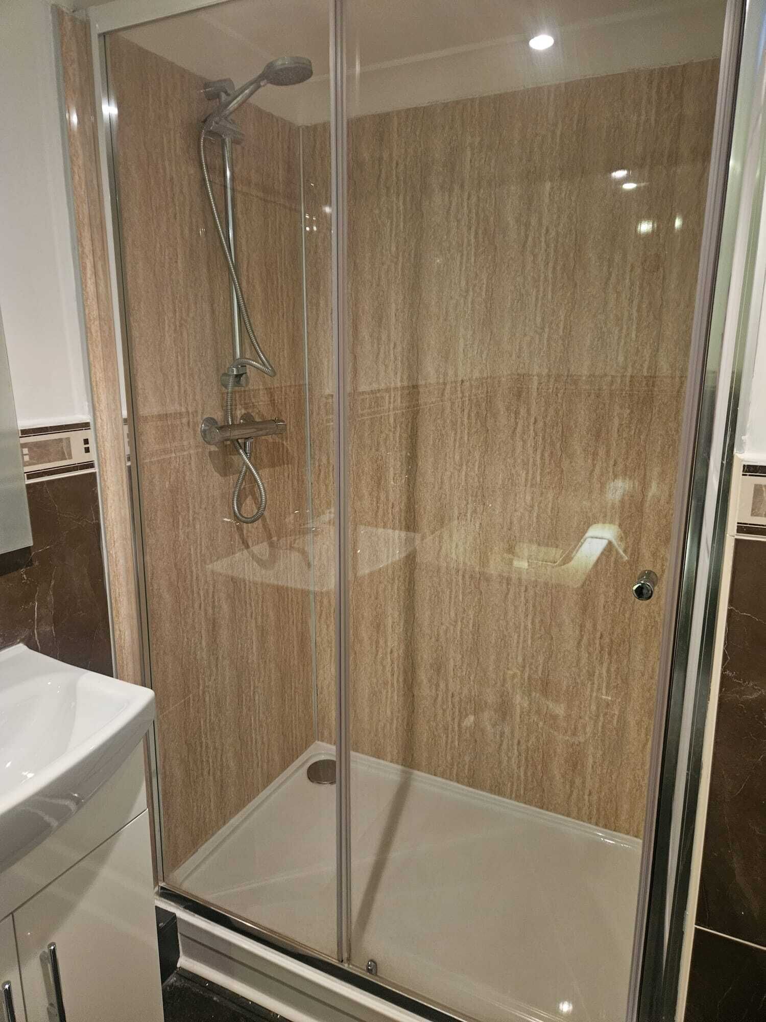 Une douche fermée par des parois en verre, dotée d’un pommeau de douche à main et d’un robinet mural.