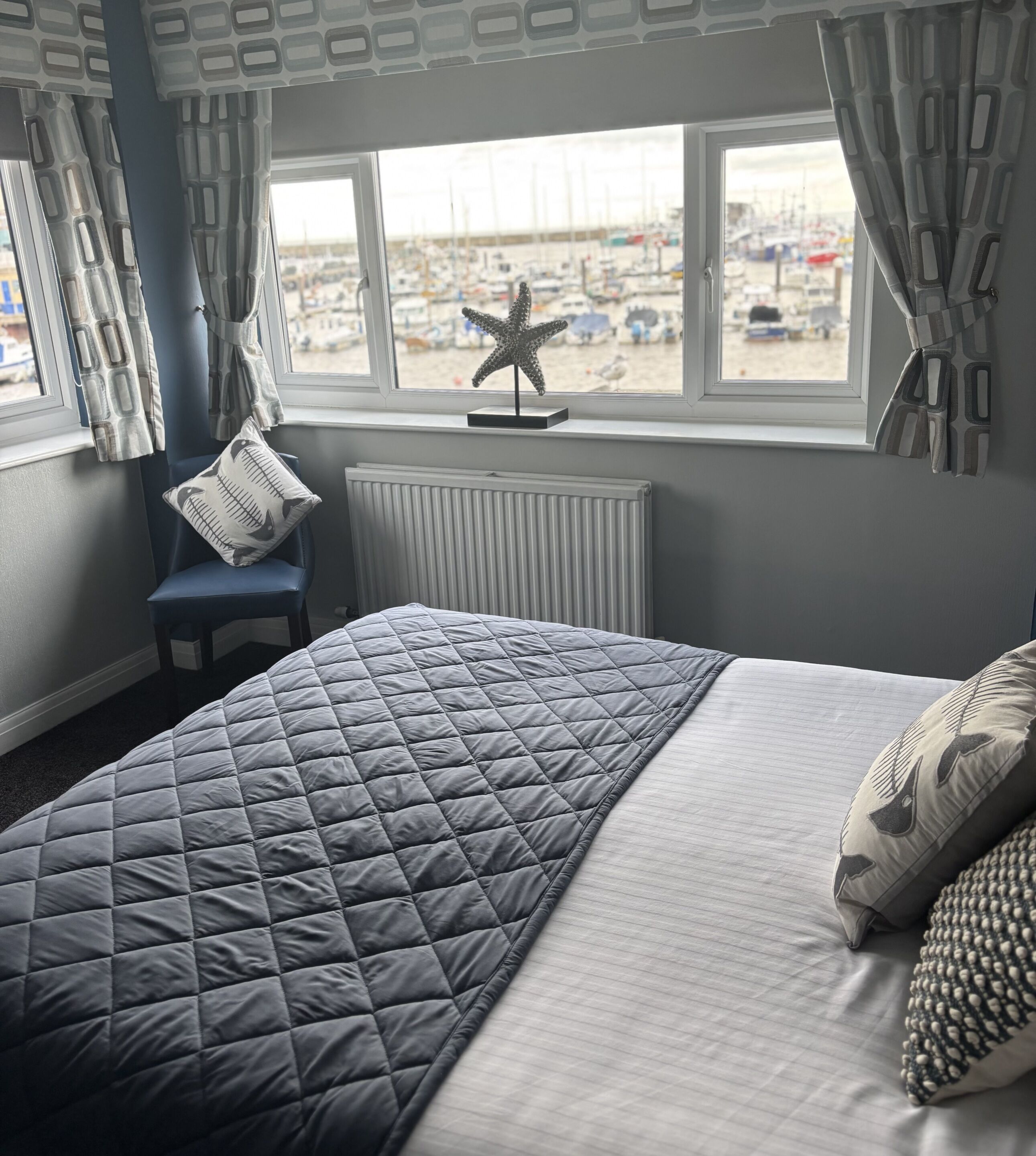 A bedroom with a bed, a chair, a radiator, a window with curtains, and a starfish decoration.