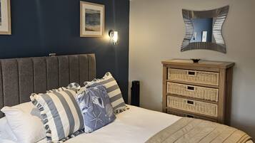 A bedroom with a bed, a headboard, a bedside table with a lamp, a mirror, and a wall-mounted light fixture.