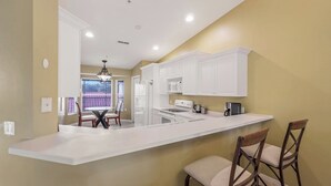 Une cuisine moderne avec des meubles blancs, un îlot central et des tabourets de bar.