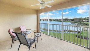 Un balcon avec une table et des chaises, un ventilateur de plafond et une vue sur un lac et des bâtiments.