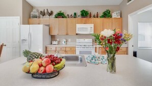 Une cuisine moderne avec des meubles en bois, un réfrigérateur blanc, un four à micro-ondes et un évier. On peut voir un panier de fruits sur le comptoir et un vase rempli de fleurs.