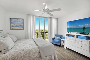 A bedroom with a bed, a chair, a TV, a ceiling fan, and a balcony with a view.