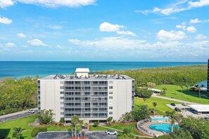 A hotel with a pool, a view of the ocean, and a parking area.