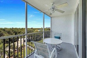 Un balcón con una mesa, sillas, ventilador de techo y vista a un paisaje verde.