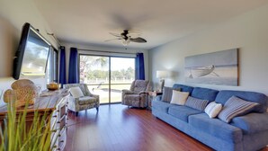 A spacious living room with a blue sofa, a wooden coffee table, and a ceiling fan. - Nautical Edgewater Resort Condo - Walk to Beaches! (Panama City Beach)