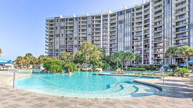 A large swimming pool surrounded by a landscaped area with palm trees and a multi-story hotel building in the background. - Nautical Edgewater Resort Condo - Walk to Beaches! (Panama City Beach)
