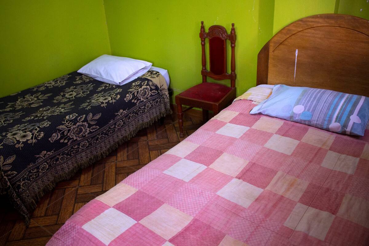 Two single beds with different bedding styles, a wooden chair, and a wooden headboard.