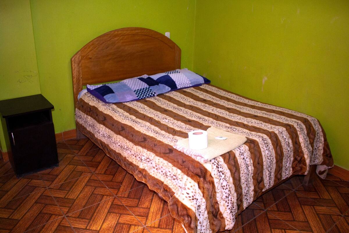A single bed with a wooden headboard, a patterned blanket, and a pillow.