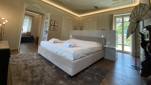 A spacious bedroom with a large bed, a ceiling with ornate designs, and a view of the outdoors through a window.