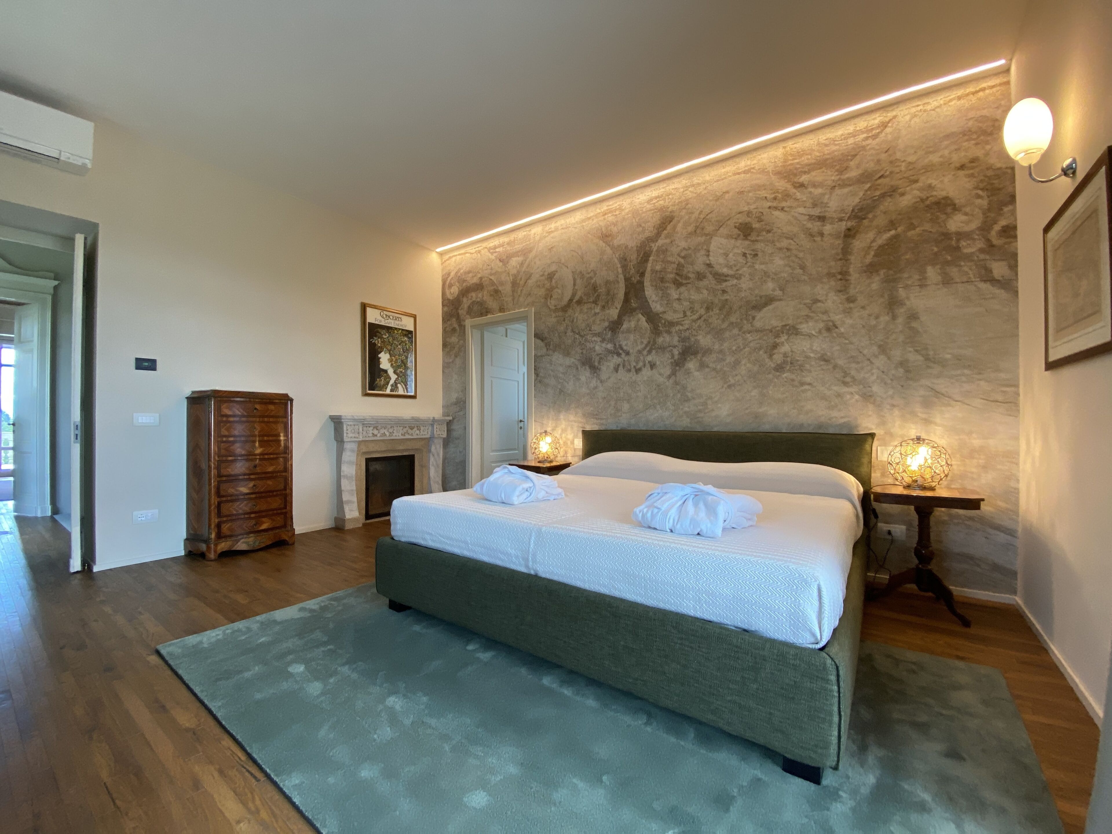 A modern bedroom with a large bed, a fireplace, and a stone wall.