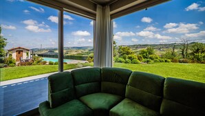 A room with a large window offering a view of a swimming pool, green lawn, and distant hills.
