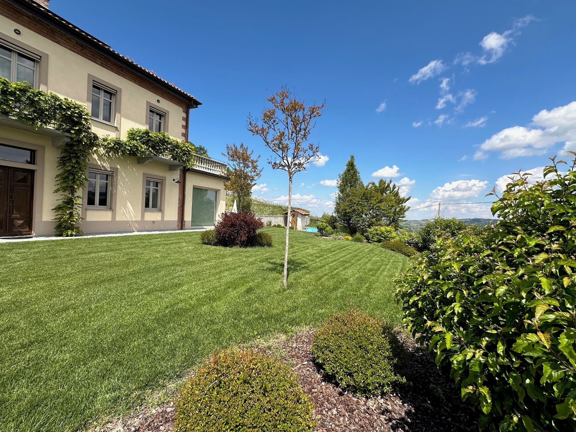 A well-maintained lawn, a house with a tiled roof, and a clear blue sky.