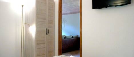 Une chambre à coucher comprenant un lit, une armoire, un téléviseur et une porte donnant sur une autre pièce.