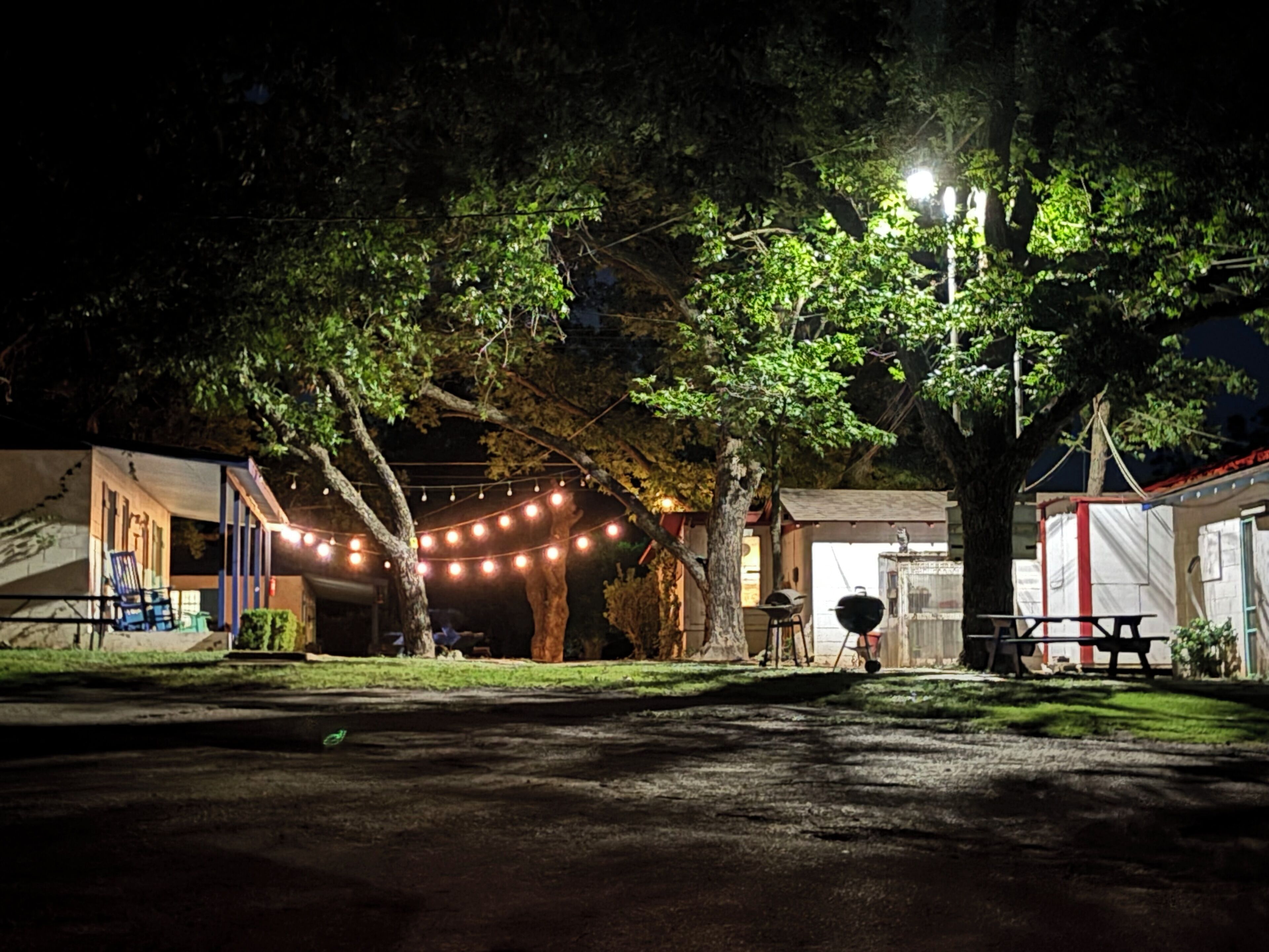 An outdoor area with string lights, a barbecue grill, and a picnic table under a large tree.