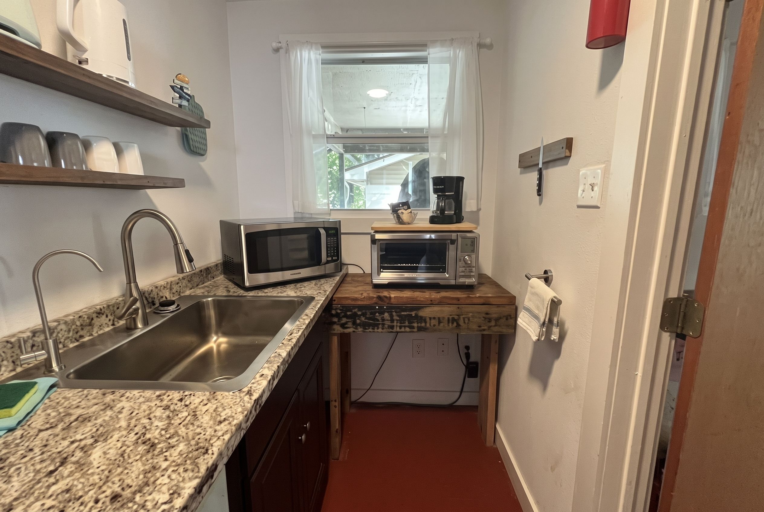 Una cocina compacta con encimera de granito, pileta de acero inoxidable y dos electrodomésticos empotrados.