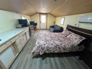 Une petite pièce comprenant un lit, un coin cuisine, une télévision et une fenêtre.