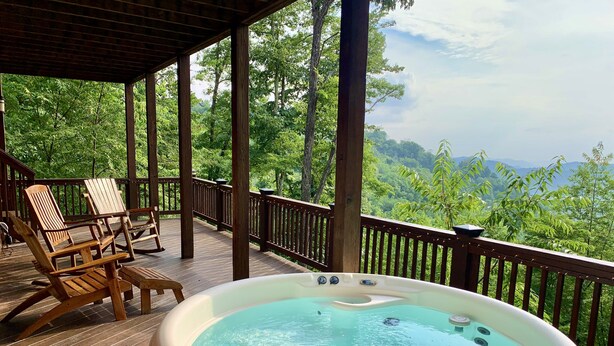 Un bain à remous sur une terrasse en bois, avec vue sur une forêt luxuriante.