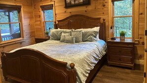 Une chambre à coucher aux murs lambrés, avec un grand lit, deux fenêtres, une table de chevet et une commode.
