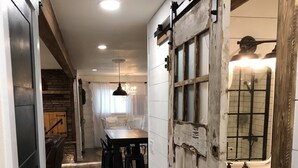 A hallway with a rustic wooden floor, a dining area with a chandelier, and a bathroom with a vintage sink.