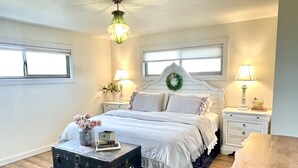 A bedroom with a bed, bedside tables, a dresser, a nightstand, a lamp, a vase with flowers, a suitcase, and a ceiling light.