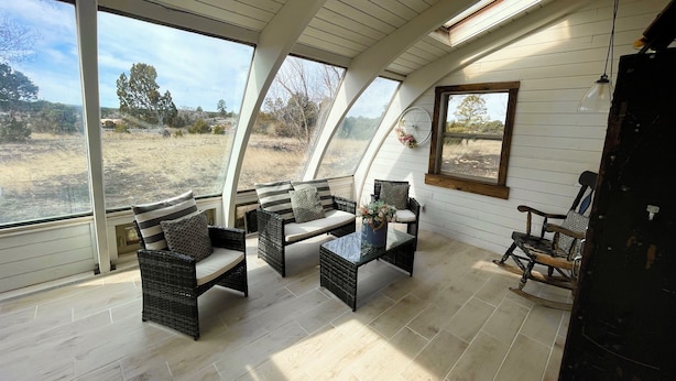 A room with a sloped ceiling, large windows, wicker furniture, and a view of the outdoors.