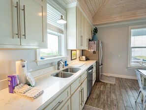 A kitchen with white cabinets, a stainless steel sink, a refrigerator, and a window with blinds.