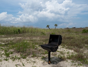 An open grill on a sandy beach with palm trees and a cloudy sky in the background.