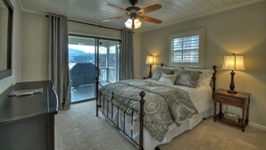 A bedroom with a bed, two bedside lamps, a ceiling fan, a nightstand, a desk, and a view through a sliding glass door to a balcony. - LAKE COTTAGE on deep water w/ incredible views! Hot tub/pool table/dock/kayaks (Blairsville)