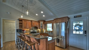 A spacious kitchen with wooden cabinets, a large island with stools, stainless steel appliances, and a white door with a window. - LAKE COTTAGE on deep water w/ incredible views! Hot tub/pool table/dock/kayaks (Blairsville)