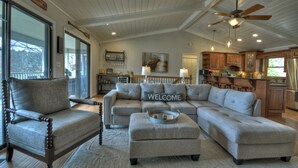 A spacious living room with a sectional sofa, a wooden chair, and a dining area with wooden cabinets and a kitchen island. - LAKE COTTAGE on deep water w/ incredible views! Hot tub/pool table/dock/kayaks (Blairsville)