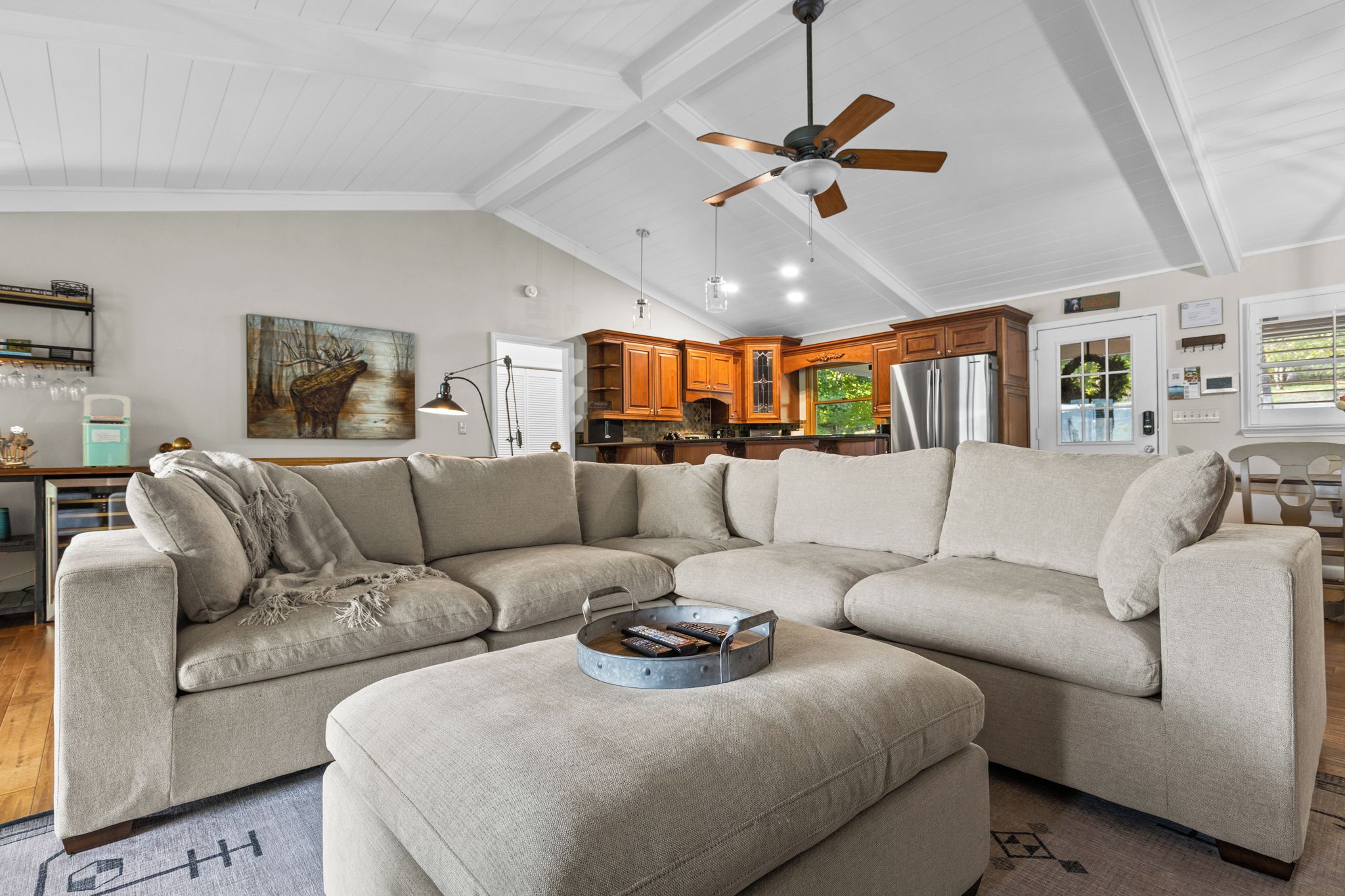 A modern living room with a sectional sofa, a coffee table with remotes, and a ceiling fan.